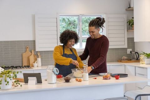 Smiling couple baking together in bright modern kitchen mixing batter on island