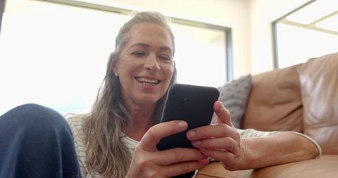 Smiling Mature Woman Relaxing with Smartphone on Couch