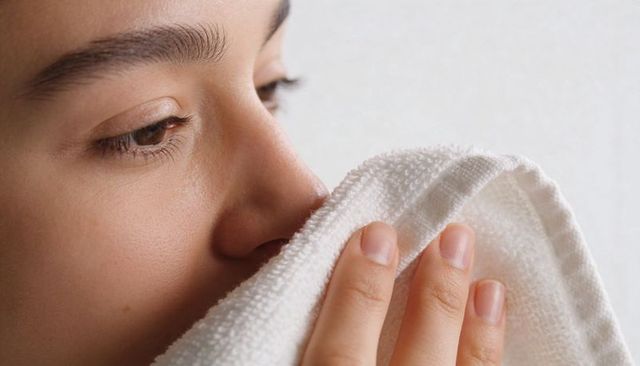 Young woman pressing white terry towel to nose and mouth for skincare self care closeup