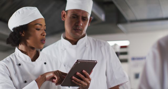 Two diverse male and female chefs talking and using tablet in restaurant kitchen. working in a busy restaurant kitchen.