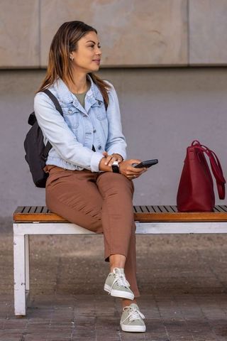 Young woman sitting on bench holding smartphone wearing denim jacket and smartwatch