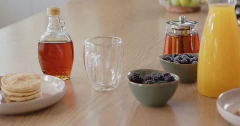 Serving cozy brunch spread with double-walled glass mug, pancakes, maple syrup and berries