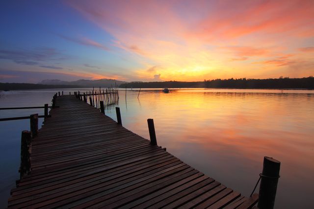 Serene wooden pier extending over calm lake waters illuminated by vibrant sunrise colors. Ideal for themes of tranquility, nature's beauty, serenity, and peaceful outdoor scenes.