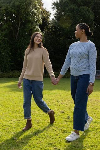 Diverse couple walking hand in hand through sunlit park wearing casual sweaters