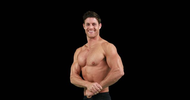 Muscular man smiling while flexing his arm against a black background. Ideal for use in fitness marketing materials, gym advertisements, health magazines, and online workout programs. Showcases a strong and healthy lifestyle, emphasizing the importance of physical fitness and bodybuilding.