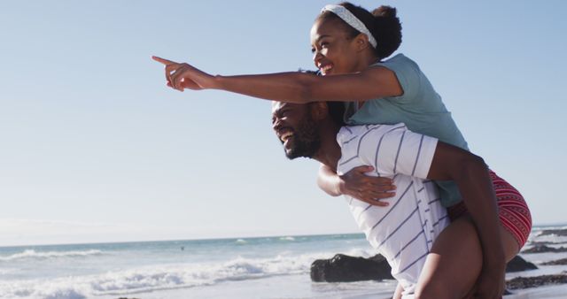 African american man smiling and carrying african american woman piggyback on the beach - Download Free Stock Photos Pikwizard.com