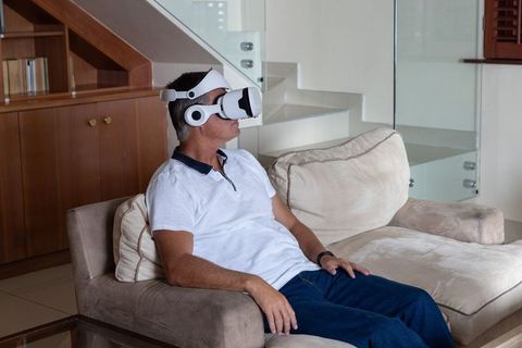 Middle-aged man wearing vr headset while relaxing on beige sofa in modern home