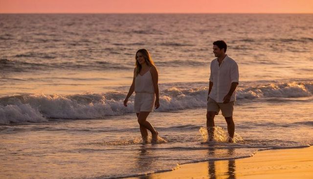Couple walking along shoreline at golden hour wearing white summer outfits