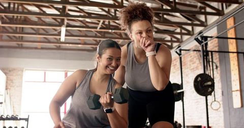 Women motivating each other while lifting dumbbells in industrial gym for strength training