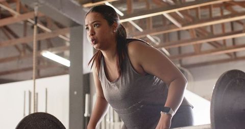 Woman in 20s preparing to deadlift loaded barbell in gym showing strength and focus