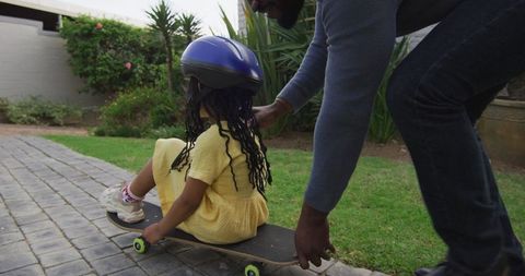 Father Guiding Daughter on Skateboard in Backyard