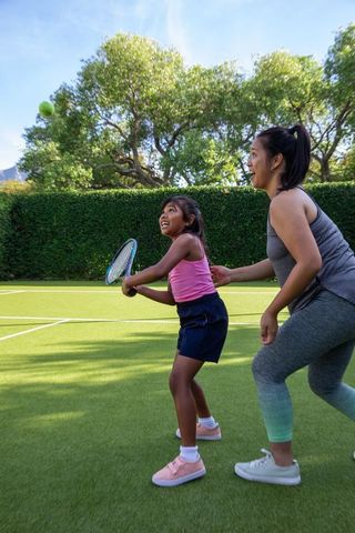 Mother teaching daughter tennis on sunny day