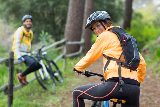 Female biker wearing helmet and backpack, riding mountain bike on forest trail. Ideal for promoting outdoor activities, adventure sports, healthy lifestyle, and fitness. Suitable for use in advertisements, blogs, and articles related to cycling, nature exploration, and women's fitness.