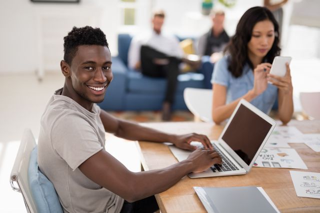 Young professionals working in a modern office setting. Male executive smiling while working on a laptop, and female executive using a mobile phone. Ideal for depicting teamwork, modern business environments, and the use of technology in the workplace.