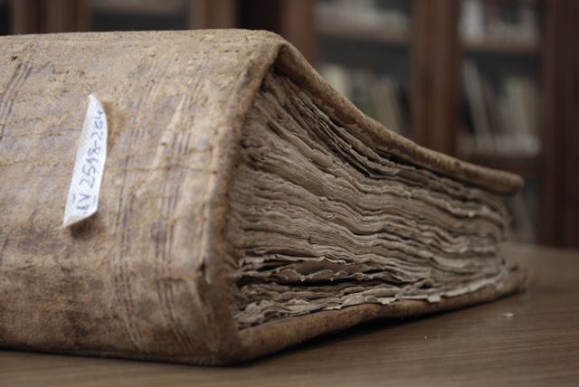This image highlights the texture and wear of an old leather-bound book resting on a wooden table. Ideal for use in articles or presentations about history, literature, or education. Suitable for library promotional materials, educational websites, and historical studies.