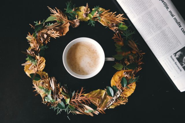 View looking down at coffee cup, adorned by autumnal wreath and accompanied by newspaper. Ideal for autumn-themed promotions, morning routines, cozy atmospheres, and coffee advertisements.