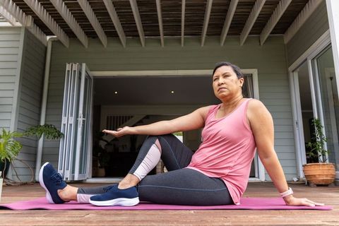 Mature woman performing seated spinal twist on wooden deck in pink activewear for wellness