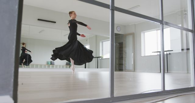 Ballet dancer in black leotard executing a graceful spin in a modern dance studio. Floor-to-ceiling mirrors and polished wooden floors enhance the sleek and professional environment. Perfect for use in articles or advertisements related to dance classes, studio promotions, performing arts, and physical fitness.