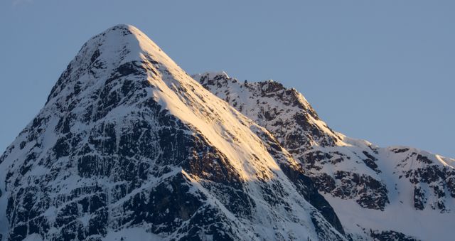 Dramatic snow-covered mountain peaks illuminated by the first light of sunrise. Ideal for outdoor adventure advertisements, travel brochures, motivational posters, or websites focused on nature and adventure.
