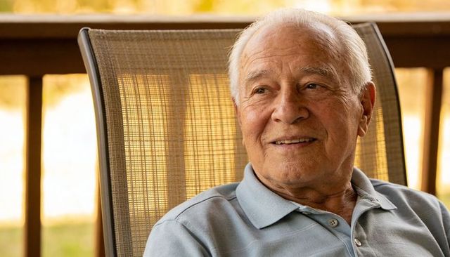 Smiling senior man relaxing on porch chair in light blue polo enjoying sunny afternoon