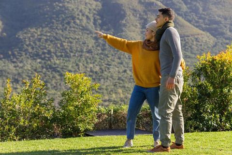 Young couple enjoying mountain view and pointing toward distant peaks on sunny hillside