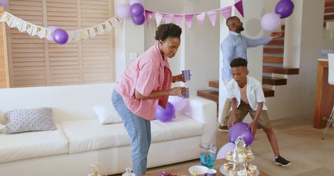 African American family decorating living room with purple balloons, cupcakes for birthday