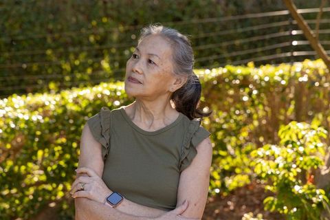 Senior asian woman enjoying sunlight in garden wearing smartwatch and olive top