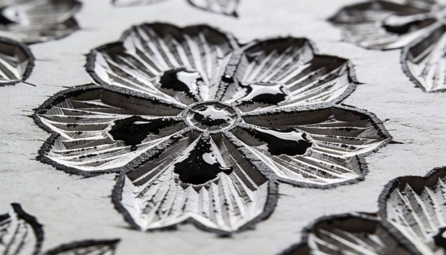 Macro detail of carved five-petal floral motif with glossy black lacquer pools on pale woodboard