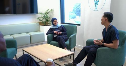 Diverse healthcare team chatting in bright lounge during coffee break, relaxed teamwork