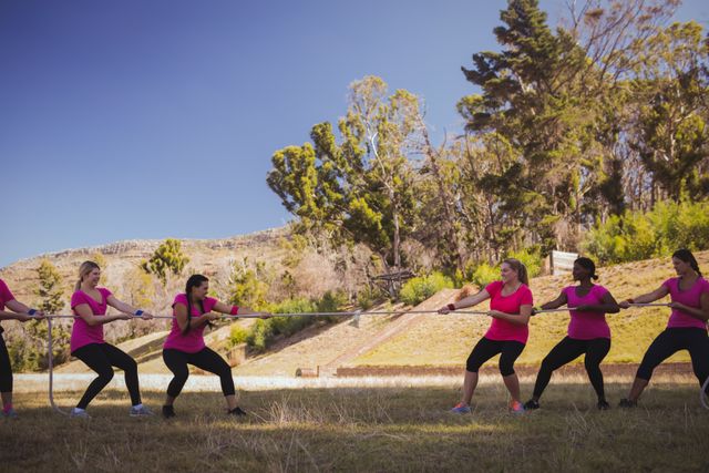 Group of women engaging in a tug of war during an obstacle course training session in a boot camp. Ideal for use in articles or advertisements related to fitness, teamwork, outdoor activities, and team-building exercises. Can also be used to promote women's sports and group fitness programs.