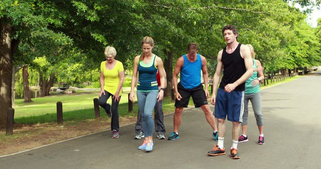 Group of individuals exercising in an outdoor park setting, demonstrating a fitness routine involving stretching and light running. Perfect for use in marketing materials for fitness programs, outdoor activity clubs, healthy lifestyle promotions, and personal training businesses. Highlighting community engagement and the benefits of outdoor physical activity.
