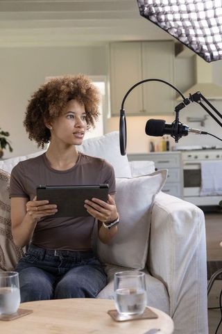 Young african american woman hosting home podcast with tablet and professional microphone