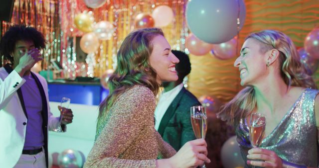 Image of two happy caucasian female friends dancing holding glasses of champagne at a nightclub. Fun, drinking, going out and party concept.