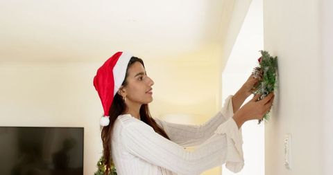 Indian woman hanging wreath wearing santa hat during christmas