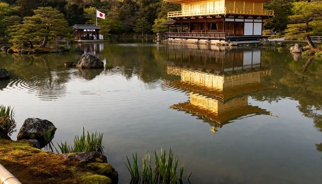 Golden pavilion reflecting on tranquil pond in japanese garden with mossy rocks and flag