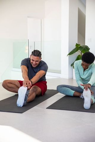 Diverse Fitness Partners Stretching on Mats in Modern Home
