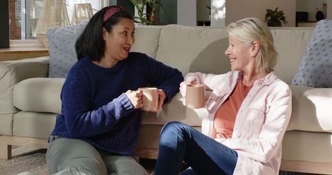 Two Diverse Female Friends Enjoying Coffee in Cozy Living Room
