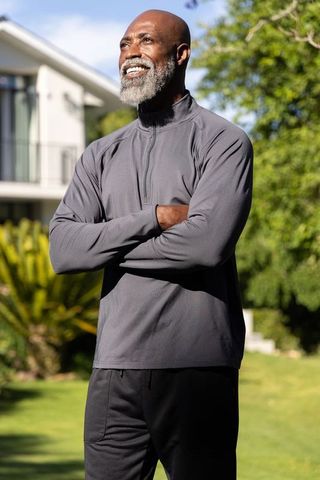Confident senior african american man standing with arms crossed in sunlit garden
