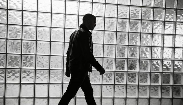 Male silhouette walking past glass block wall in corridor wearing leather jacket