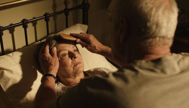 Senior man brushing partner's hair in bed, tender nighttime caregiving and companionship