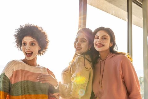 Diverse friends enjoying at-home spa day wearing facial masks and cozy knits in sunlight