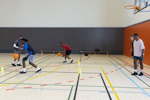 Multiethnic men practicing basketball dribbling drills on indoor court with cones and coach