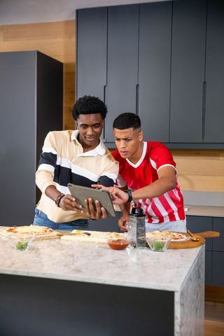 Two Male Friends Making Homemade Pizzas in Modern Kitchen
