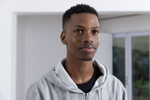 Young Man in Gray Hoodie at Home with Natural Light and Greenery Views