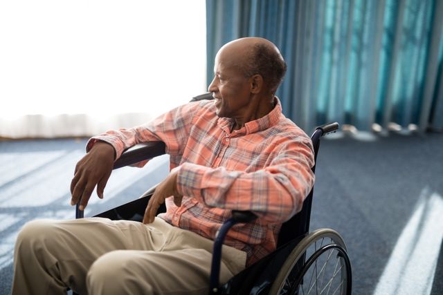Senior man sitting in wheelchair, smiling and looking content. Ideal for use in healthcare, retirement home promotions, elderly care services, and lifestyle articles focusing on senior independence and well-being.
