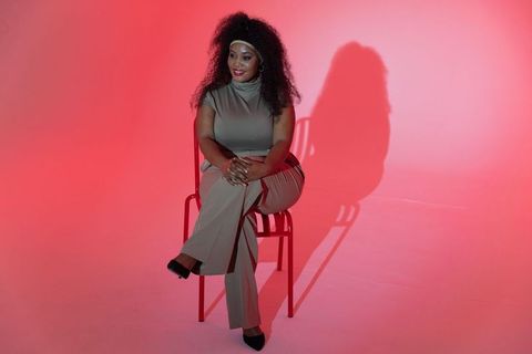 Confident african american woman sitting on red chair against pink gradient backdrop