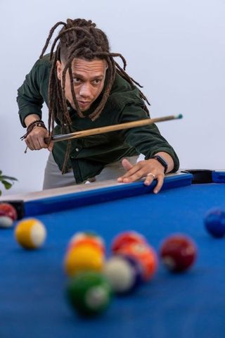 African american man leaning and aiming cue on blue-felt pool table focusing shot