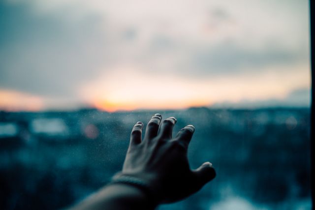 A hand with extended fingers is reaching out toward the blurred background of a sky at sunset or sunrise. Great for concepts related to hope, aspirations, freedom, dreams, and emotional states like longing or yearning. Can be used in motivational and inspirational contexts or materials.