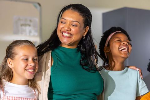 Teacher bonding with diverse preteens smiling and embracing in bright classroom
