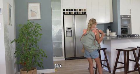 Young girl wearing backpack at modern scandinavian kitchen island with stainless fridge